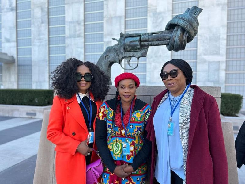 Three women posing in front of a sculpture outside an international venue